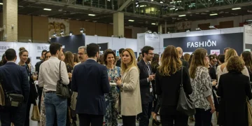 Profesionales de la moda interactuando en un evento vibrante en España, con stands y pasarelas de fondo.