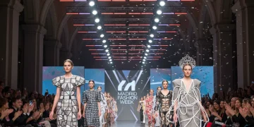 Modelos desfilando en una pasarela de alta costura, luces brillantes y público atento en un evento de moda en España.